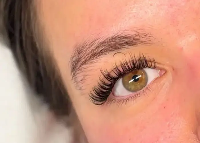 Close-up of a client's open eye with a full, wispy set of dark lash extensions, curling up and out towards the outer corner.