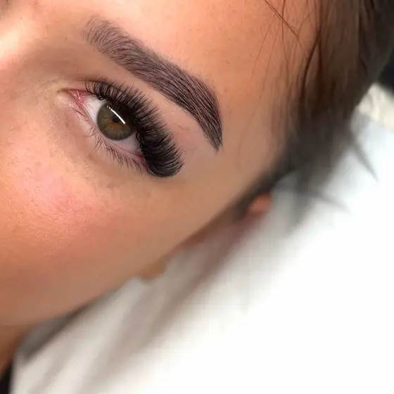 A client lying back with a full set of dark lash extensions and freshly shaped, tinted brows.