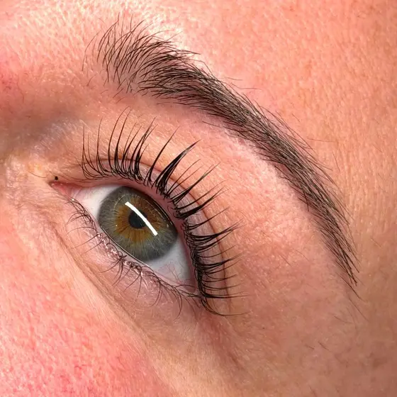 Close-up of natural lashes lifted and curled from the root after a lash lift, with a hazel eye looking up.