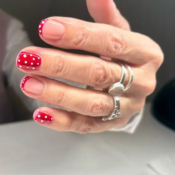 A hand with short, glossy nails: red with white polka dots on two, and red-tipped French on the others.
